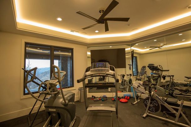 Mirrored home gym with cardio equipment and ceiling fan