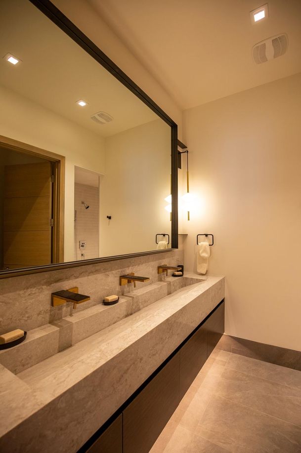 Sleek bathroom with long trough sink and gold faucets