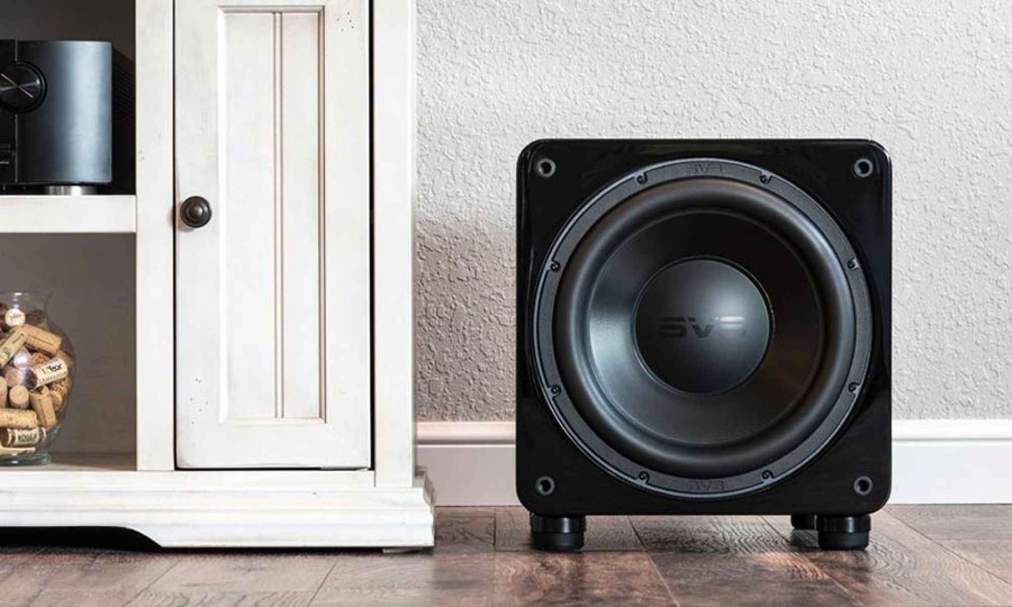Compact subwoofer placed beside a cabinet on a hardwood floor